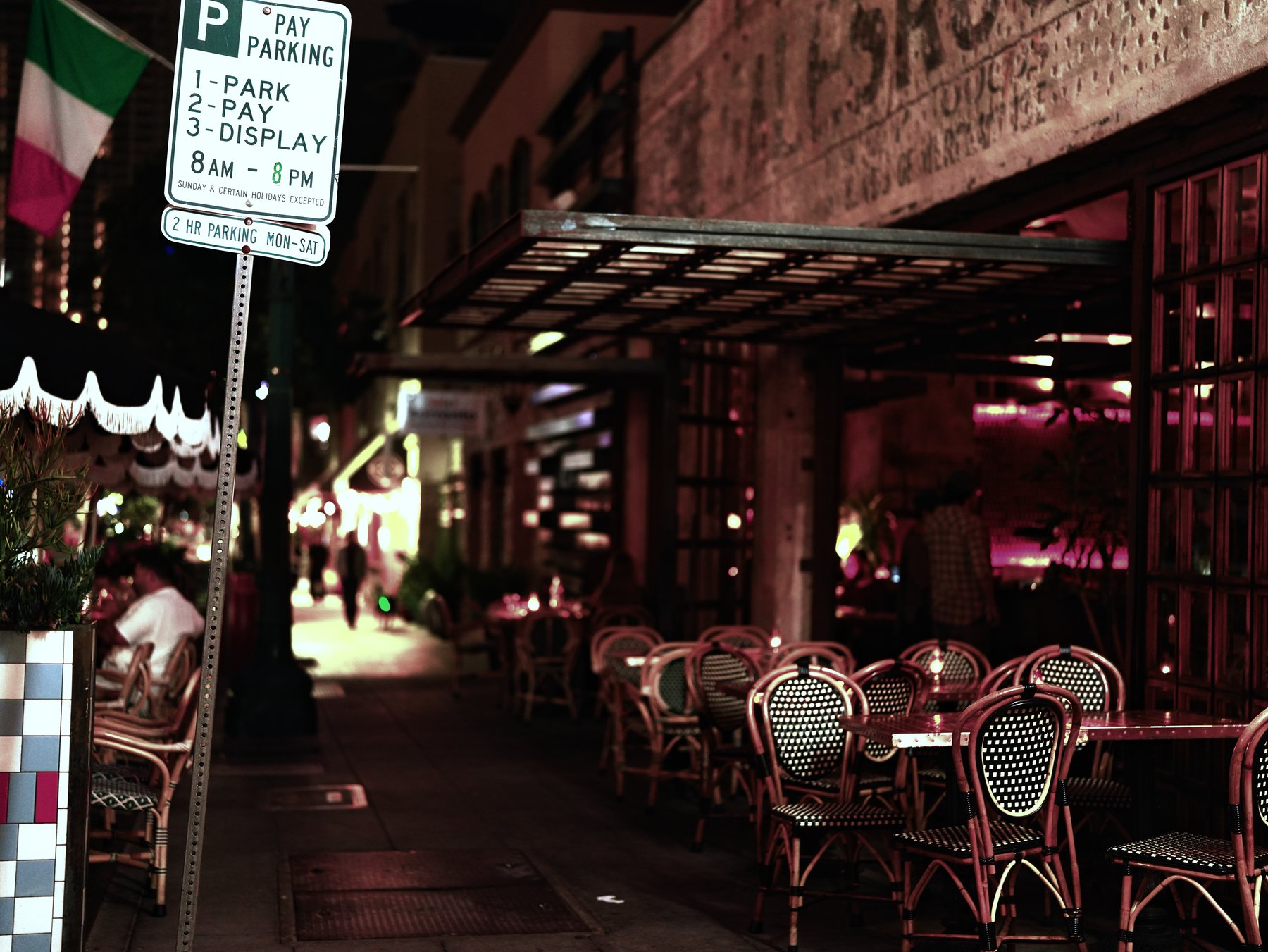 Sidewalk cafe at night with woven bistro chairs beneath an awning — photograph by Wayne Anderson