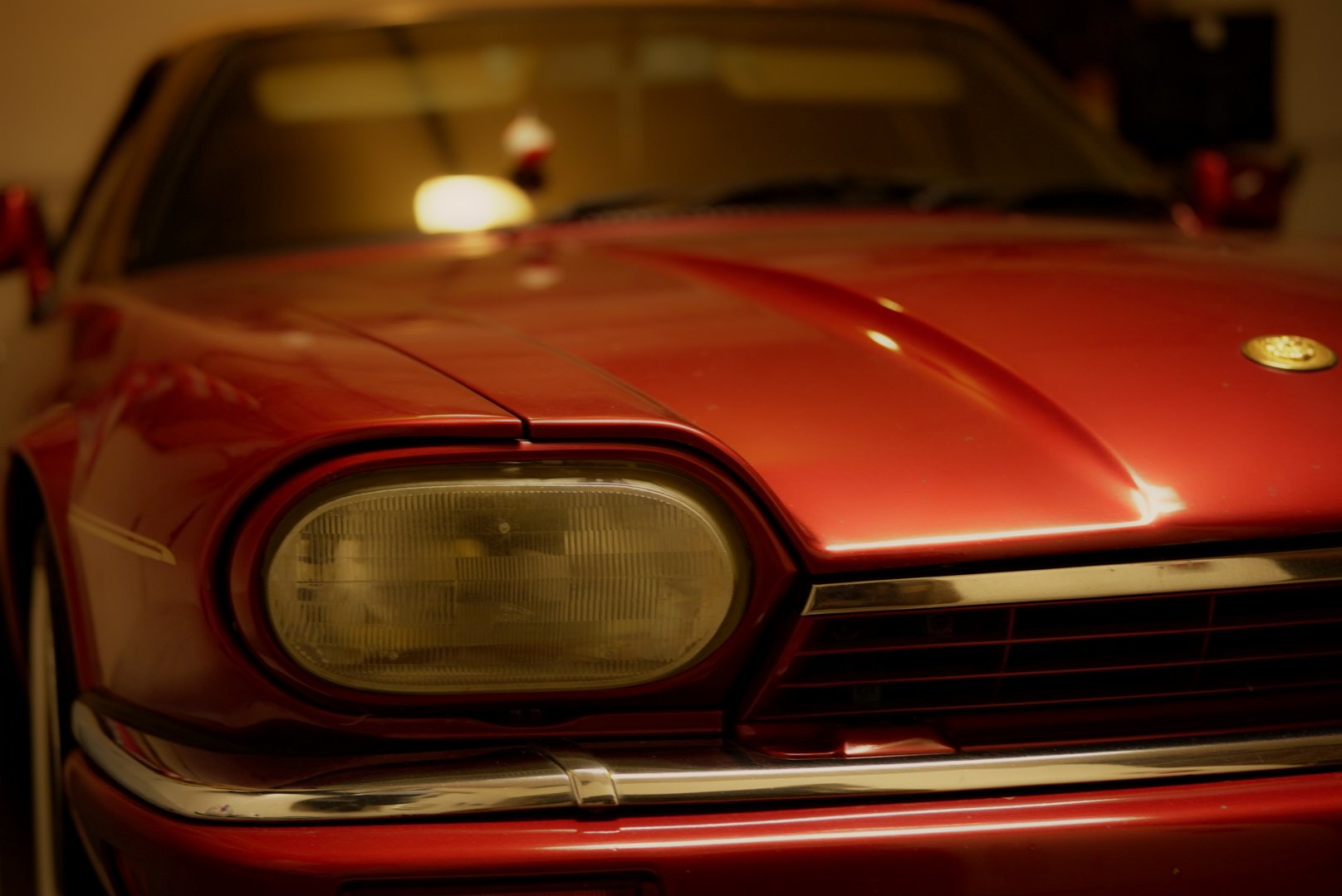 Close-up of a classic red Jaguar headlamp in warm evening light — photograph by Wayne Anderson