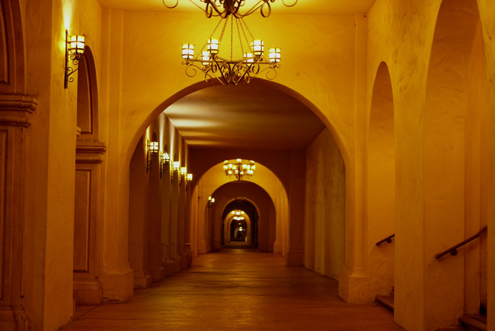 Amber-lit arched colonnade at night, chandeliers receding down the corridor — photograph by Wayne Anderson